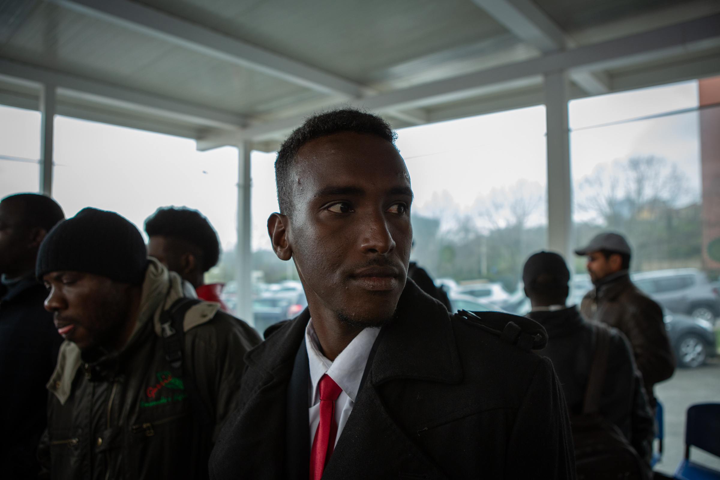 Abdirahman awaits in an exterior waiting area for the opening of the Ragusa Central Police Station on March 20, 2019.